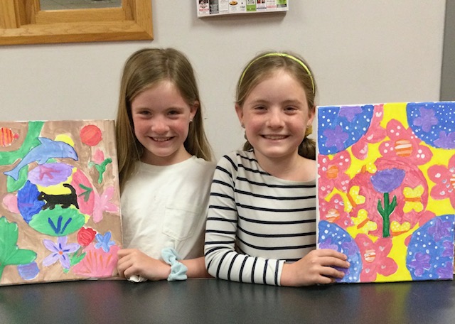 Twin elementary school girls displaying the paintings they've made